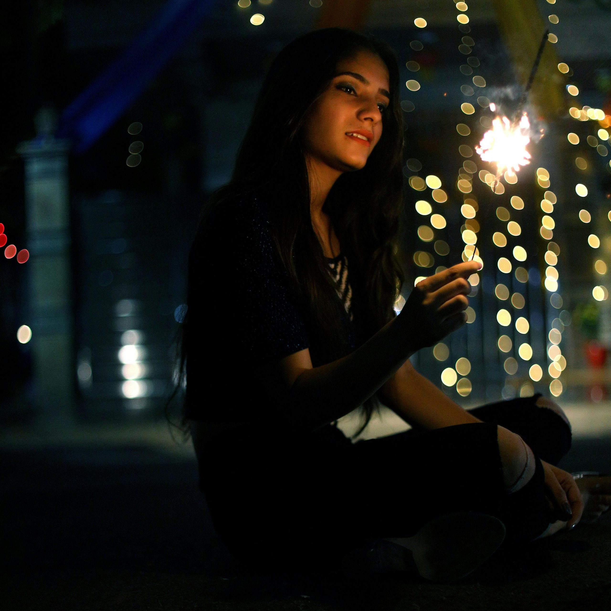 A young woman holding a sparkling sparkler, creating a festive atmosphere at night.